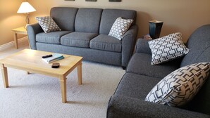 A living room with a grey sofa, two patterned pillows, a wooden coffee table, and a lamp. - Quiet condo at beautiful Mabel Lake (Enderby)