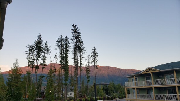 A pool area with a view of mountains, a multi-story building with balconies, and golf carts parked nearby. - Quiet condo at beautiful Mabel Lake (Enderby)