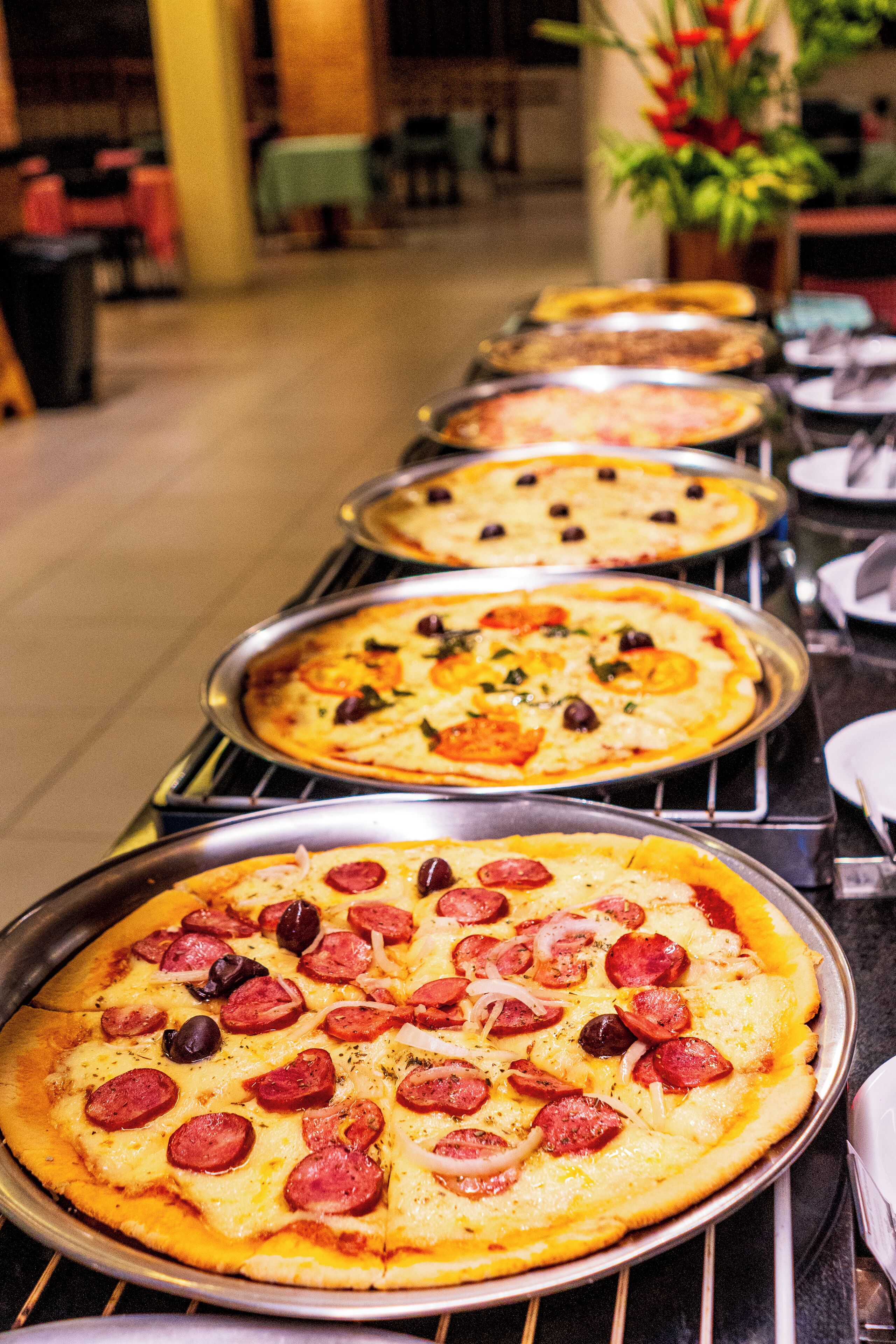 A row of pizzas on trays, likely in a dining area.
