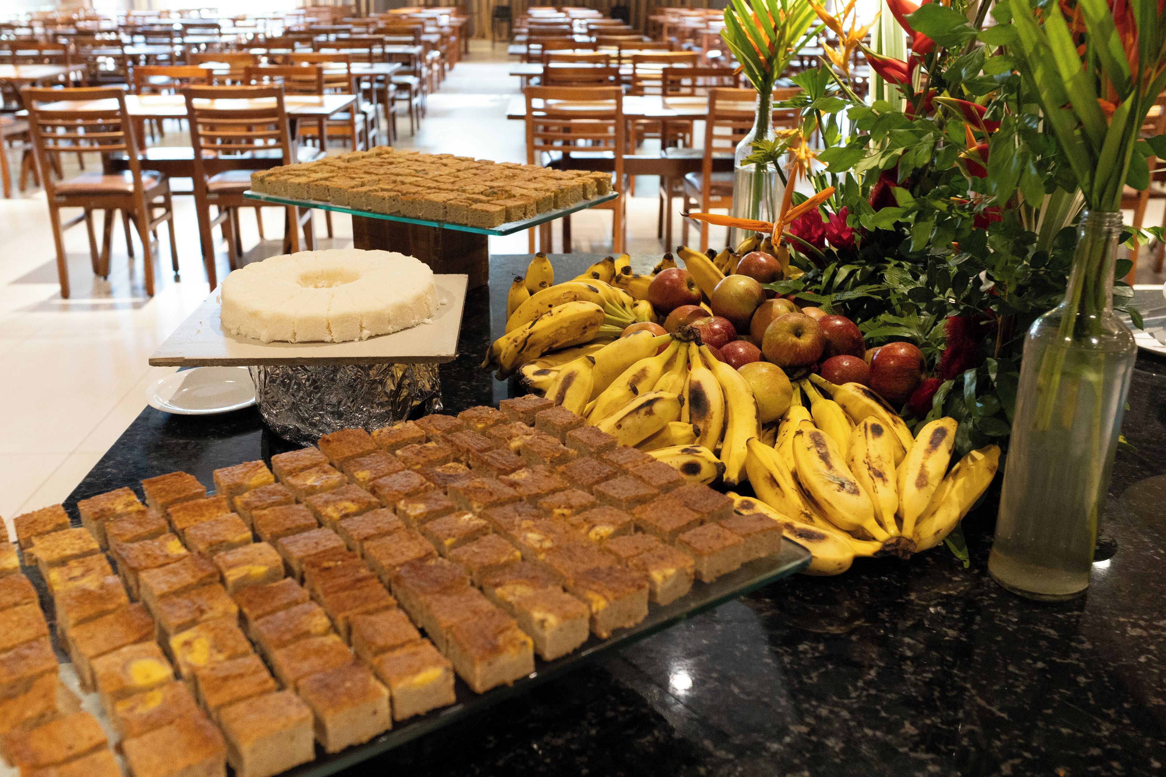 A buffet table with various food items including a cake, bananas, apples, and a floral arrangement.