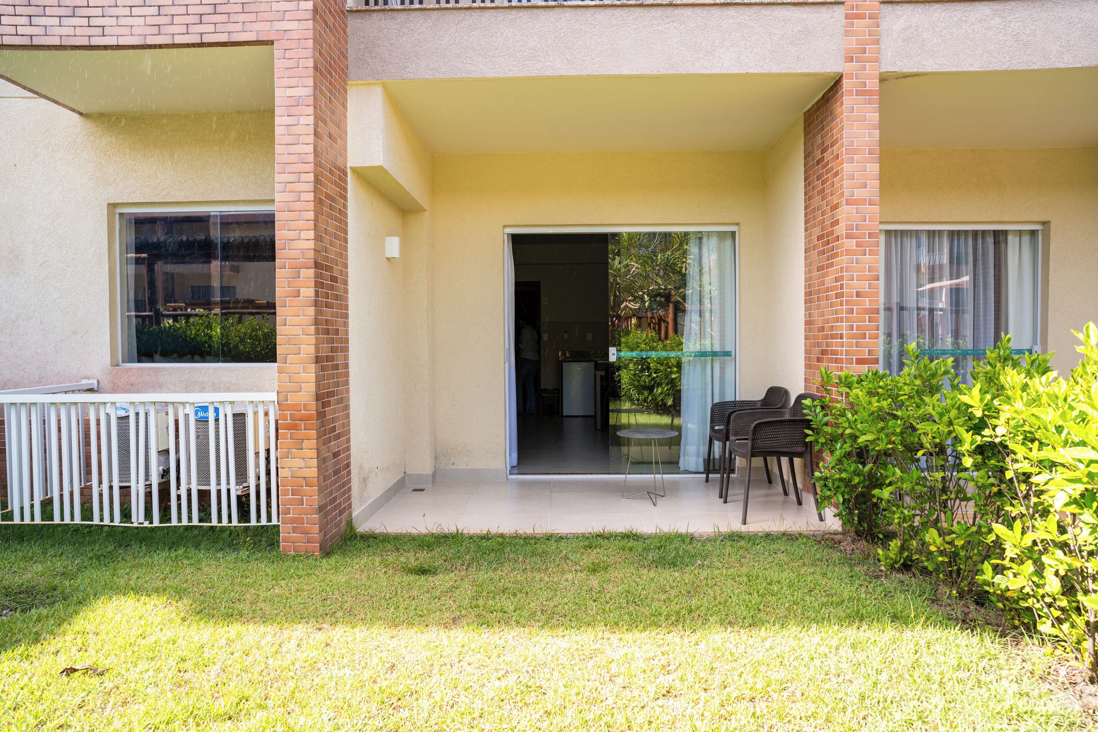 Um edifício com área externa coberta, um pequeno jardim e uma porta que dá para o interior.