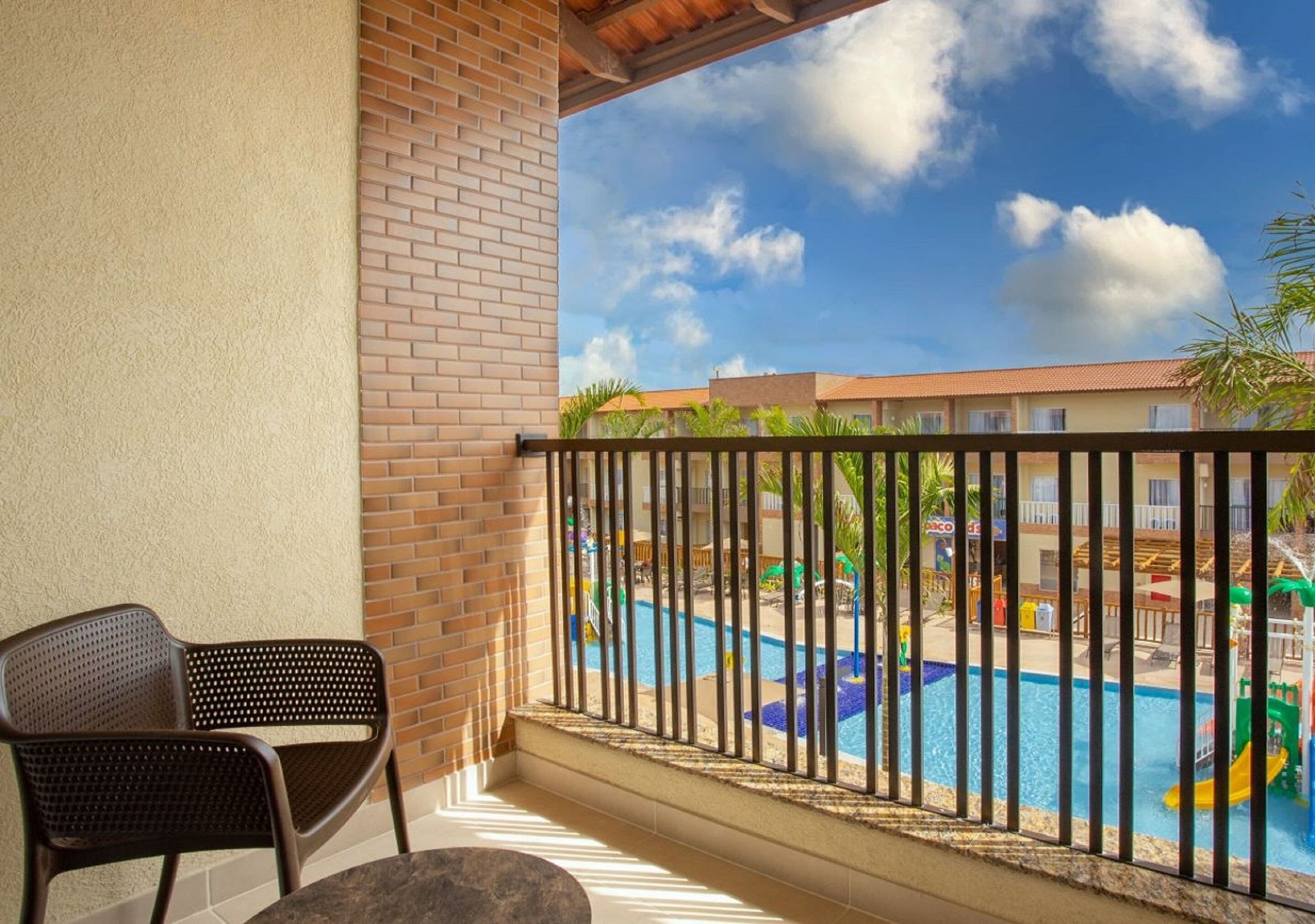 A balcony with a view of a swimming pool and a brick wall.