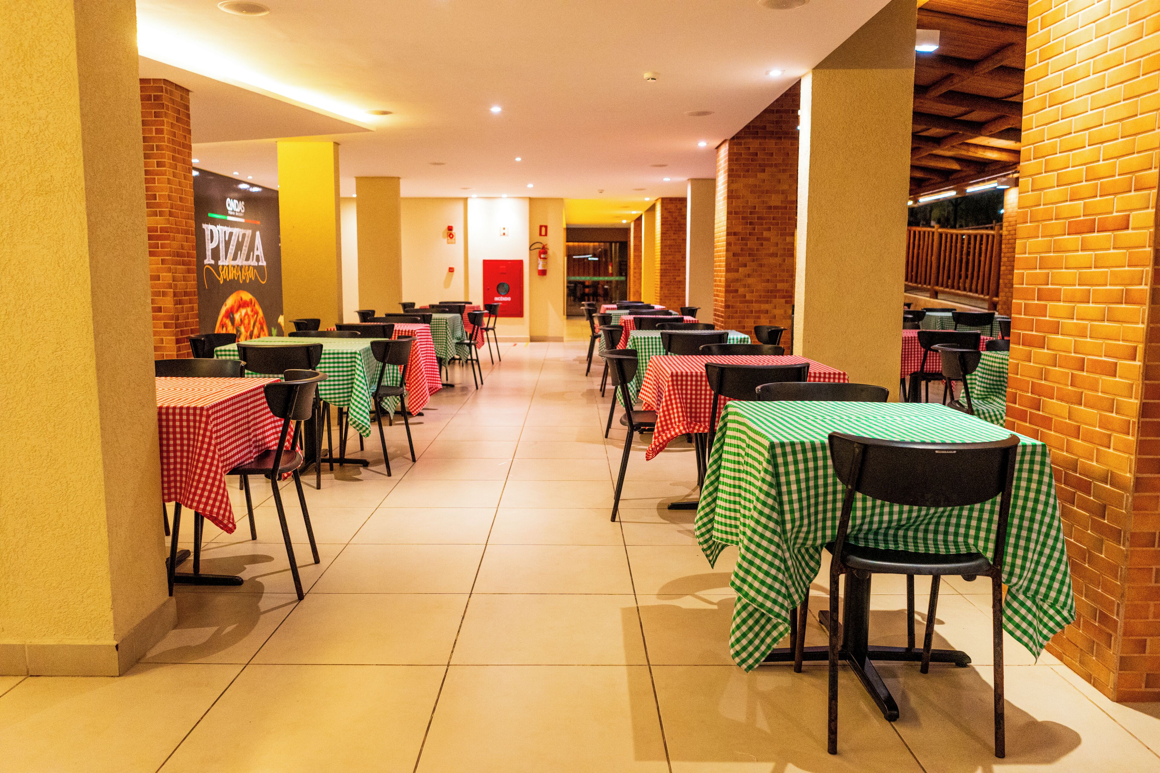 Un ristorante con diversi tavoli e sedie, caratterizzato da un muro in mattoni e un cartello con la scritta pizza.