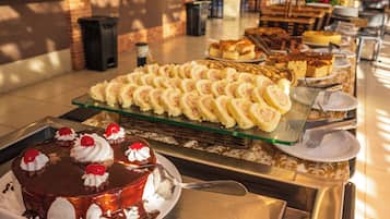 A buffet with various desserts including a chocolate cake with whipped cream and cherries, and a selection of pastries and cakes on a glass serving tray.