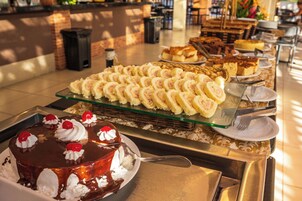 A buffet with various desserts including a chocolate cake with whipped cream and cherries, and a selection of pastries and cakes on a glass serving tray.