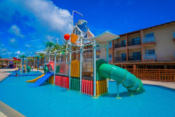 A water park with slides and play structures, surrounded by a pool and a building with balconies.