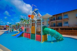 Un parque acuático con toboganes y estructuras de juego, rodeado por una piscina y un edificio con balcones.