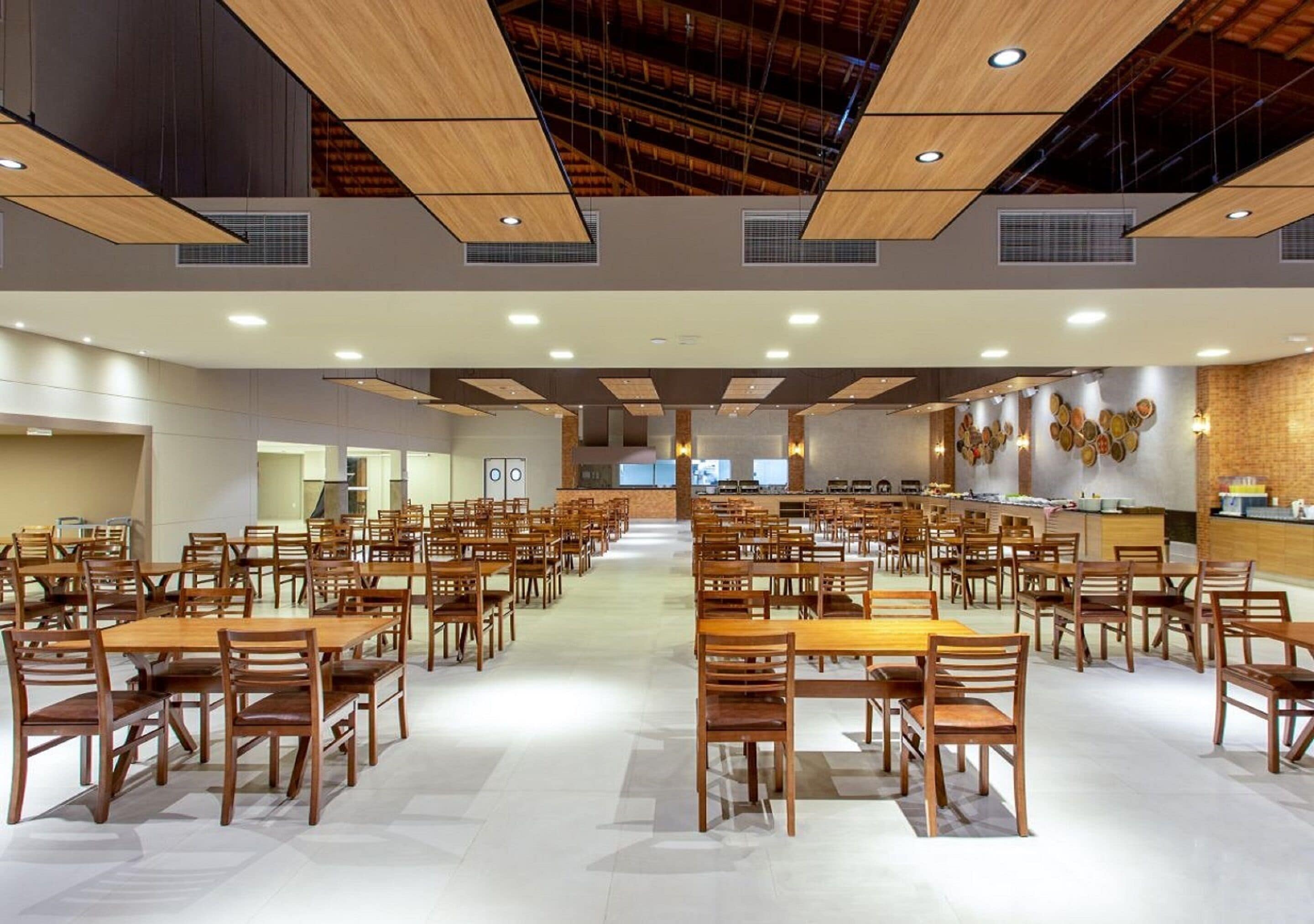 A spacious dining area with multiple tables and chairs, wooden ceiling beams, and a brick wall with decorative plates.