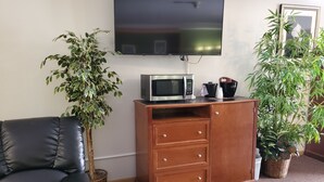 A living room with a flat-screen TV, a microwave, a wooden cabinet, a black leather chair, and two potted plants. - Bryan Inn (Bryan)