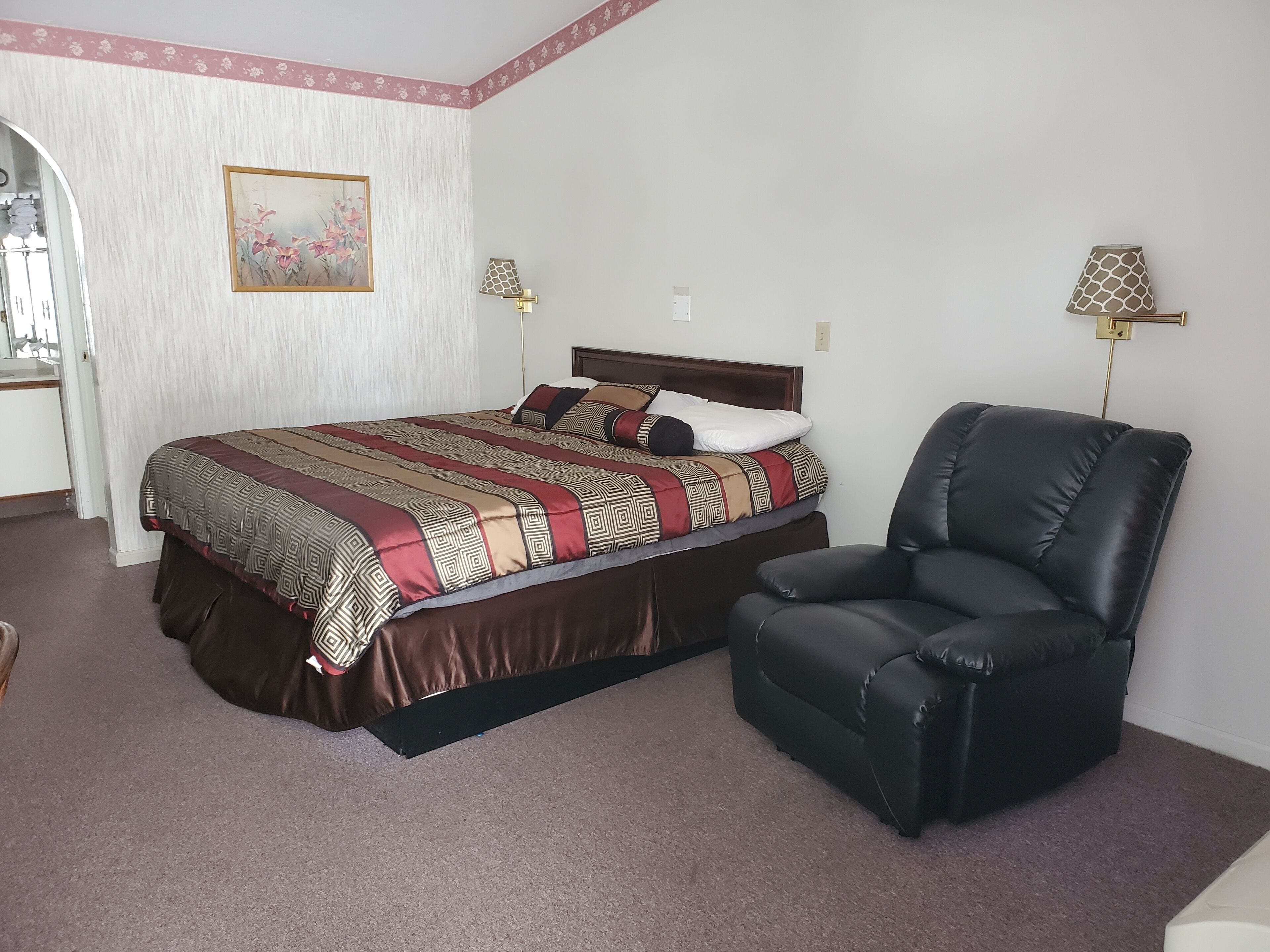 A neatly arranged bedroom with a large bed, a black leather chair, and two wall-mounted lamps.