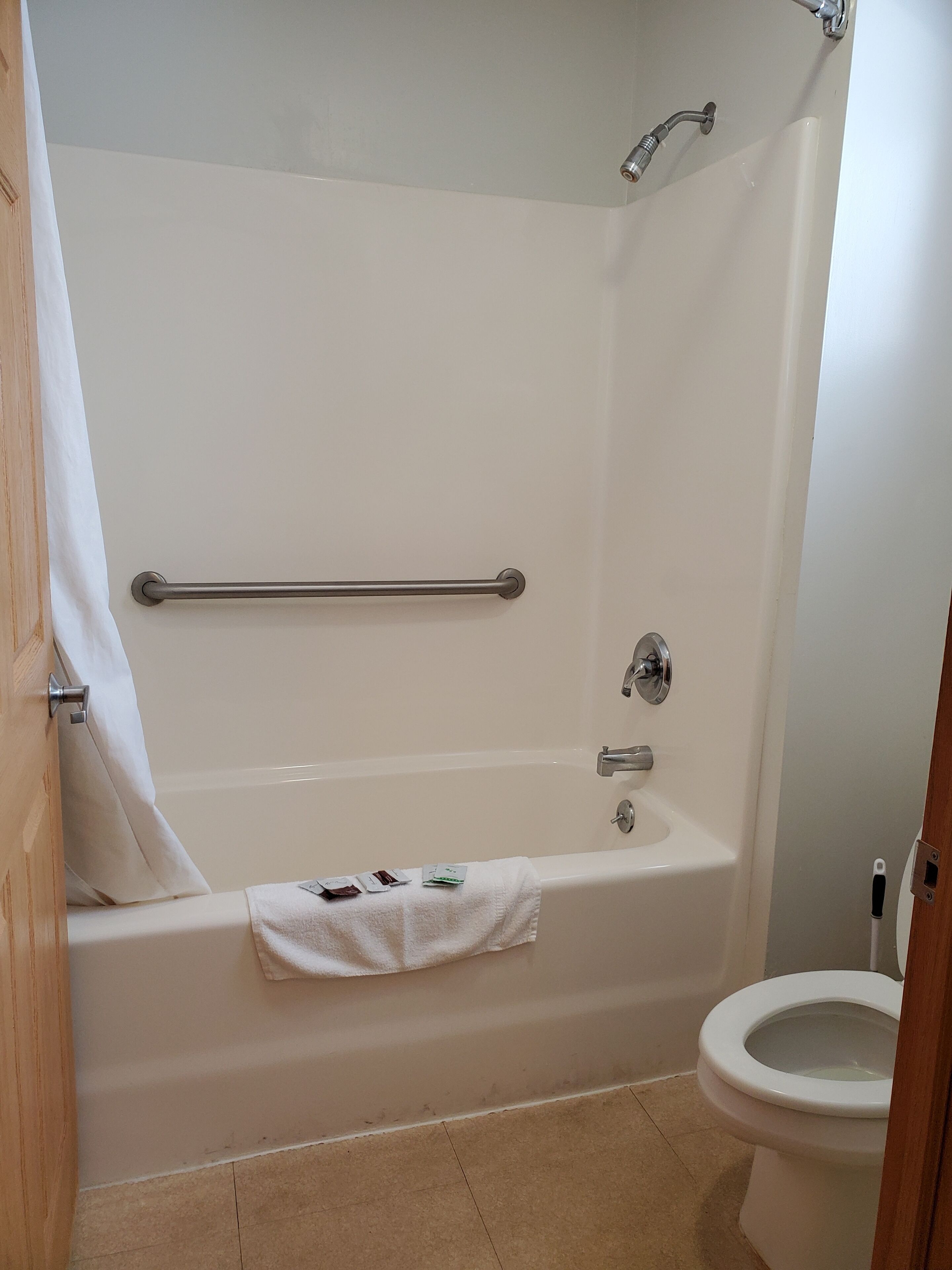 A bathroom with a bathtub, toilet, and a handrail.