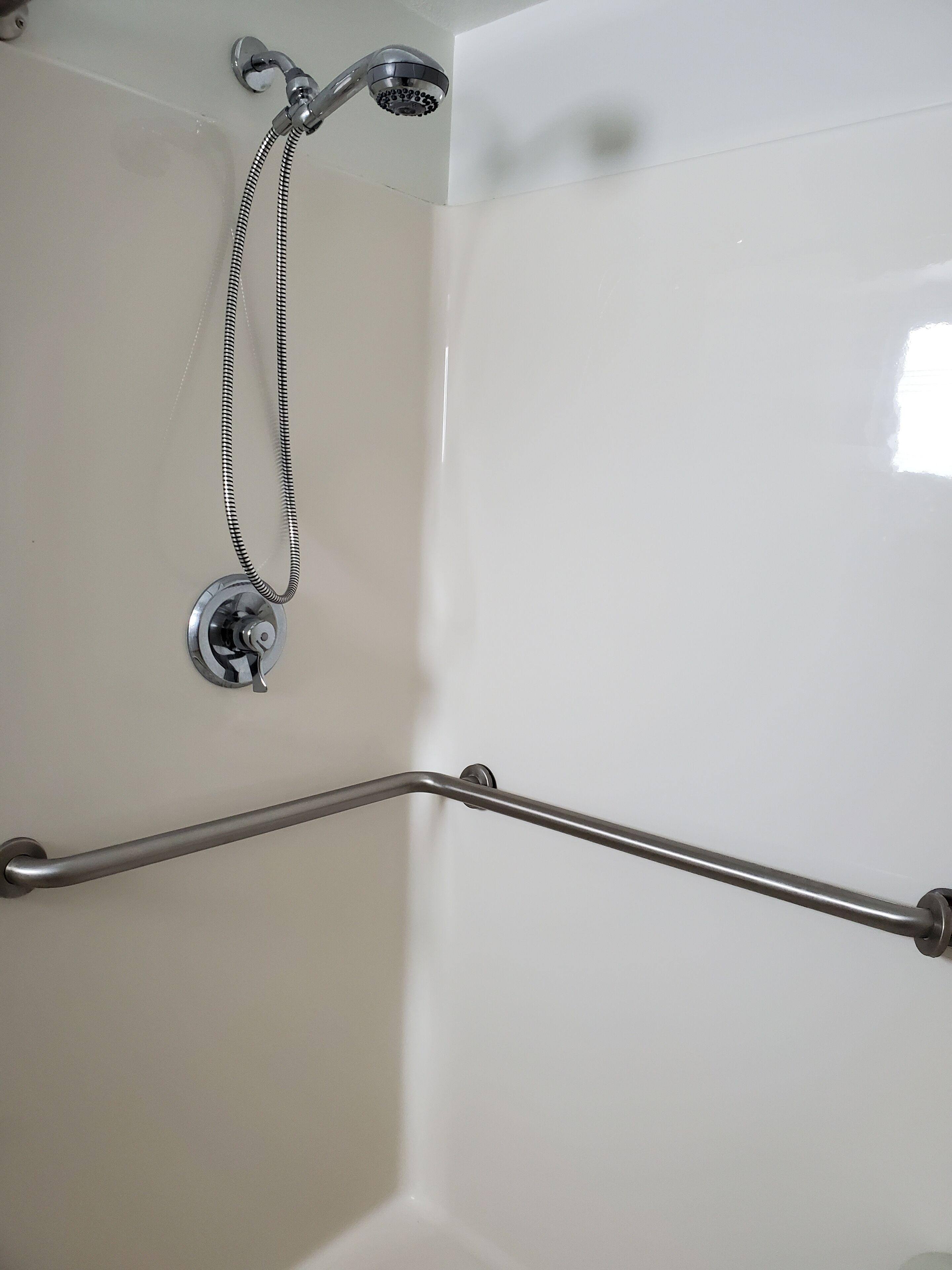 A bathroom with a shower, a grab bar, and a wall-mounted faucet.
