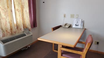 A room with a table, a chair, an air conditioner, a telephone, and a wall socket.