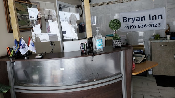 A hotel reception desk with a sign for Bryan Inn, a phone, a cash register, and flags on the left. - Bryan Inn (Bryan)