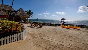 A beach with thatched-roof huts, a wooden fence, and kayaks. - El Gran Castillo de Arena (San Pedro)