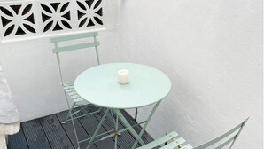 Un pequeño espacio al aire libre con una mesa redonda y dos sillas, una vela blanca sobre la mesa y una pared decorativa blanca con recortes geométricos.