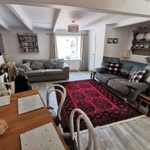 A living room with a sofa, a red patterned rug, a bookshelf, and a dining area with chairs and a table.