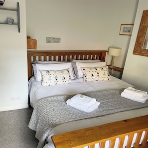 A bed with a wooden headboard, two pillows with nautical patterns, a grey textured bedspread, and a folded white towel on the bed.