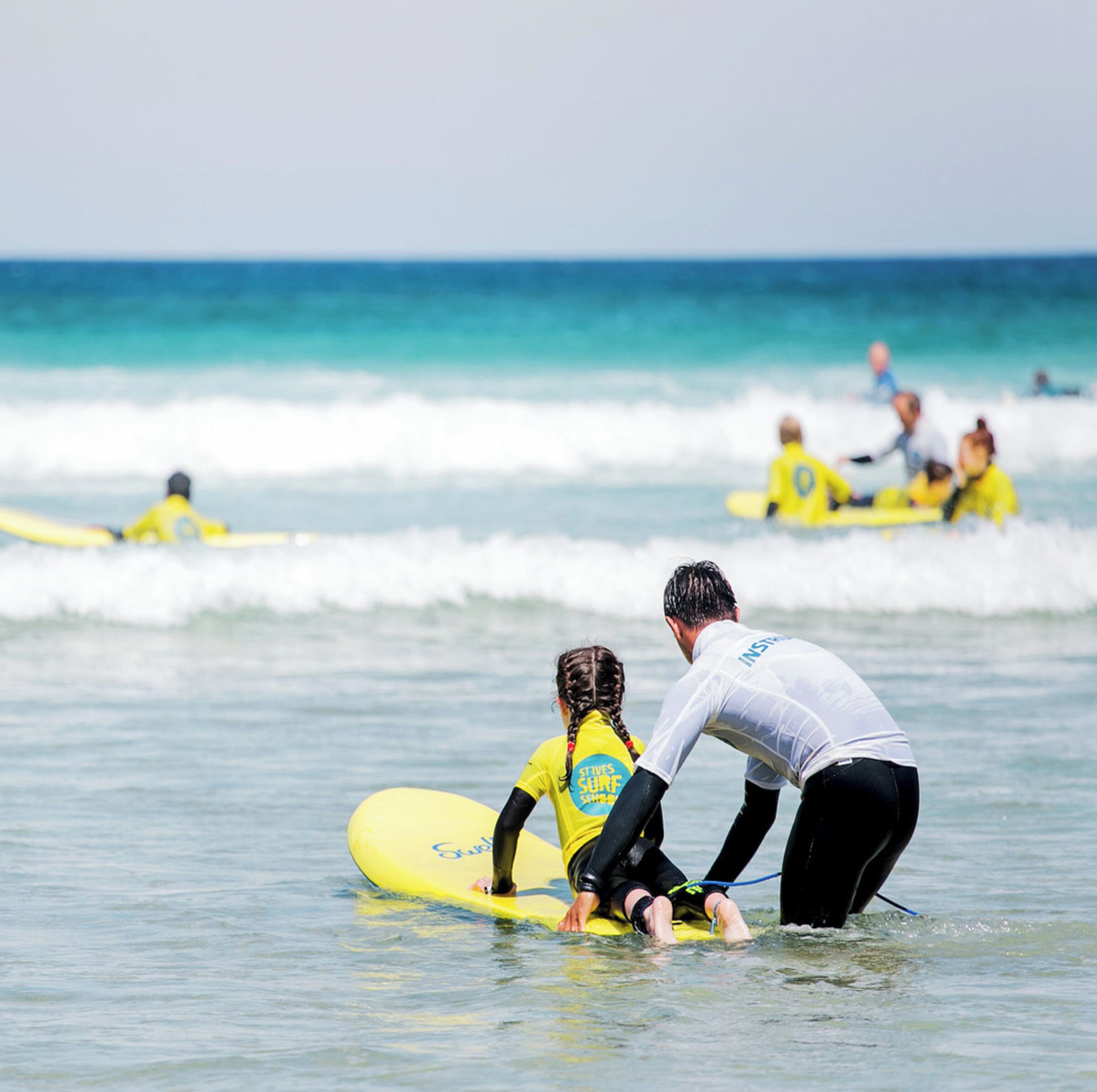 A beach scene with people on surfboards, a clear sky, and calm ocean waves.