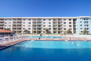 Ein Hotel mit großem Schwimmbad, mehreren Balkonen und blauem Himmel.