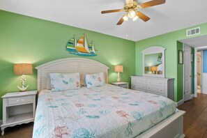 Ein Schlafzimmer mit einem Bett, Nachttischen, einem Schminktisch und einem Deckenventilator, mit einer Dekoration eines Segelboots an der Wand.