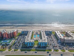 Luftaufnahme eines Küstenhotels mit mehreren Gebäuden, einem Parkplatz und einem Strand.