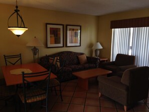 Cozy living space with a sofa set, dining table, and side table, featuring a window with vertical blinds.