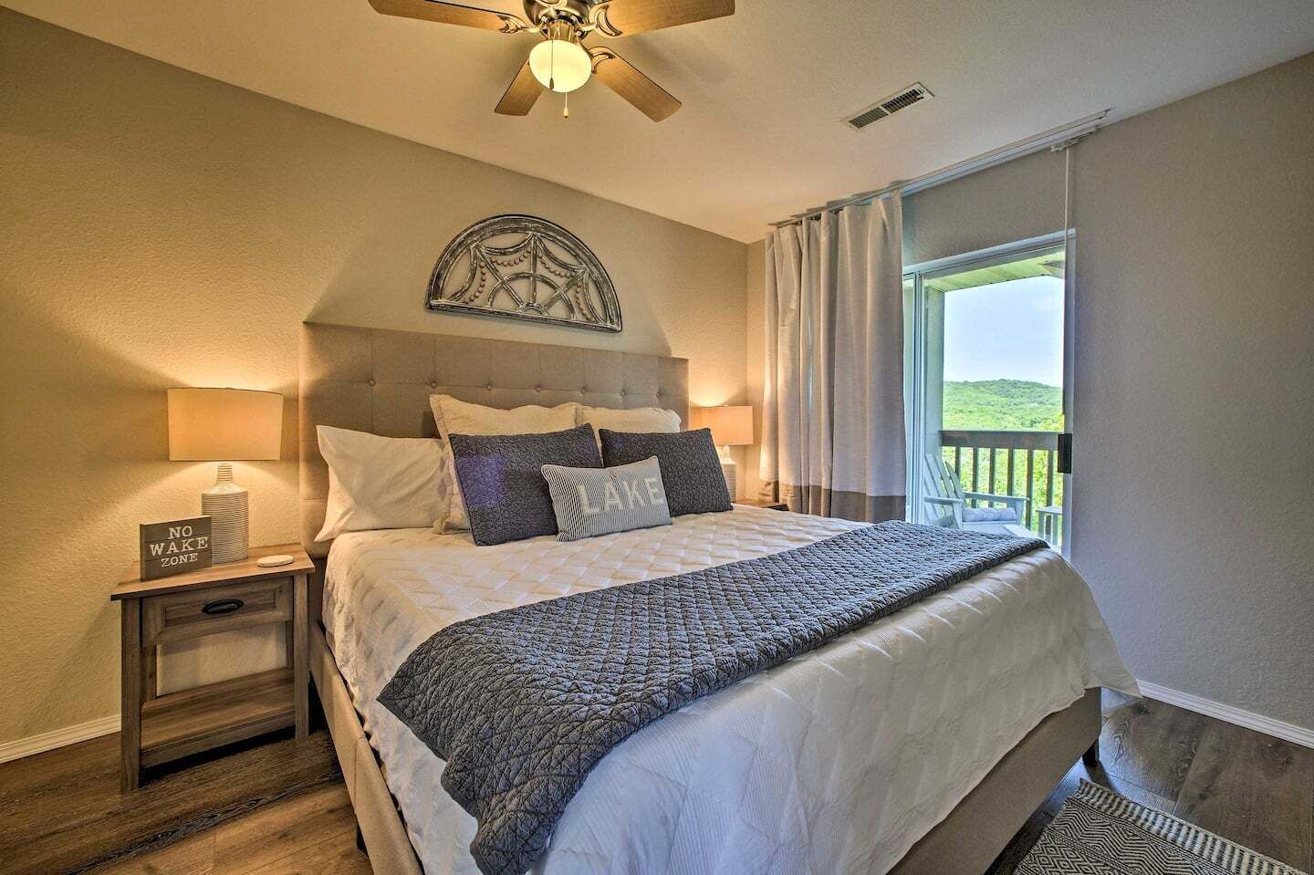 Une chambre avec un grand lit, une table de chevet avec une lampe, un élément décoratif mural et une vue sur un balcon.