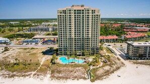 A high-rise hotel with a central courtyard featuring a swimming pool, surrounded by palm trees and a beach. - Grand Panama 904 Gulf Front & Pet Friendly, Sleeps 9 (Panama City Beach)