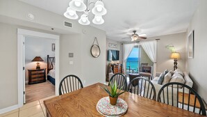 A dining area with a wooden table, chairs, a potted plant, and a view of the ocean. - Grand Panama 904 Gulf Front & Pet Friendly, Sleeps 9 (Panama City Beach)