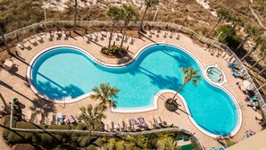 An aerial view of a resort pool with a unique shape, surrounded by lounge chairs and palm trees. - Grand Panama 904 Gulf Front & Pet Friendly, Sleeps 9 (Panama City Beach)