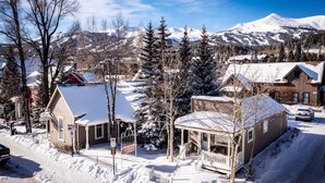 A snow-covered residential area with houses, a wooden cabin, and a mountain in the background. - Downtown Breck~7BR&7BA~Walk to Gondola~Hot Tub~AC~3 Parking Spots (Breckenridge)