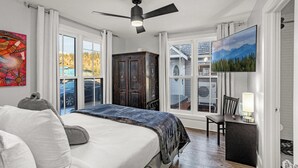 A bedroom with a large bed, a ceiling fan, a TV, and a view of the outdoors. - Downtown Breck~7BR&7BA~Walk to Gondola~Hot Tub~AC~3 Parking Spots (Breckenridge)