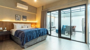 A modern hotel room with a large bed, a desk, and a sliding glass door leading to a balcony with seating. - Charlie Oscar Freire (São Paulo)