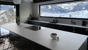 Eine moderne Küche mit einer großen Kochinsel, einem Fenster mit Blick auf die Berge und Pendelleuchten.