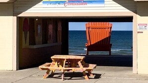 A beachside concession with a sign reading "Sunset Side" and a wooden table with chairs in front. - IN TOWN, ONLY 3 BLOCKS FROM LAKE MICHIGAN’S “STEARNS BEACH”! (Ludington)