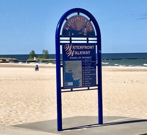 A signboard titled "Ludington Waterfront Walkway" listing points of interest like Stearns Park, Beach & Lighthouse, and City Hall. - IN TOWN, ONLY 3 BLOCKS FROM LAKE MICHIGAN’S “STEARNS BEACH”! (Ludington)