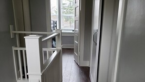 A narrow staircase with white railings and a dark wooden floor leading to a room with a window. - IN TOWN, ONLY 3 BLOCKS FROM LAKE MICHIGAN’S “STEARNS BEACH”! (Ludington)
