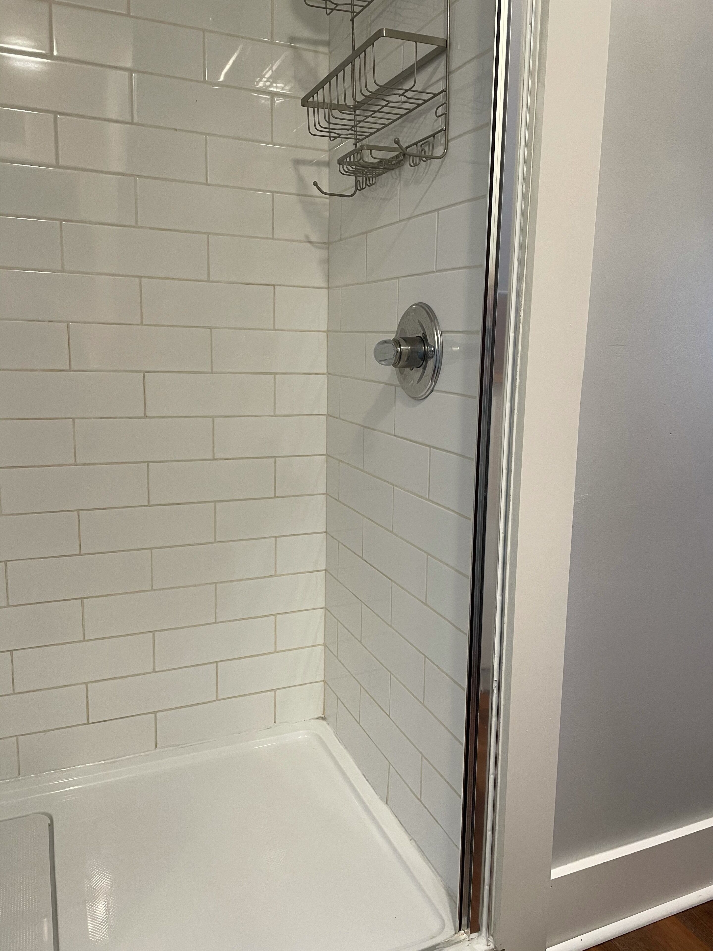 Une salle de bain avec des murs recouverts de carreaux blancs, un espace douche et une porte de douche en verre.