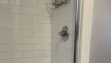 Une salle de bain avec des murs recouverts de carreaux blancs, un espace douche et une porte de douche en verre.