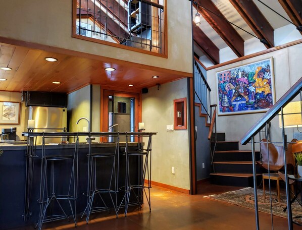 A spacious kitchen with a bar area, a staircase, and a large painting on the wall. - Monthly Rental- The Architect's Annex in the Bozeman's Downtown Brewery District (Bozeman)