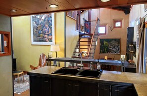 A kitchen with a large island, a dining area with a table and chairs, a staircase, and a painting on the wall. - Monthly Rental- The Architect's Annex in the Bozeman's Downtown Brewery District (Bozeman)
