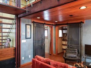 A spacious room with a wooden ceiling, a red sofa, a black leather chair, and a TV on a stand. - Monthly Rental- The Architect's Annex in the Bozeman's Downtown Brewery District (Bozeman)
