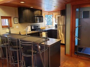 A kitchen with a central island, bar stools, stainless steel appliances, and a sliding door. - Monthly Rental- The Architect's Annex in the Bozeman's Downtown Brewery District (Bozeman)