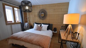 Un dormitorio con una cama grande, cabecera de madera, un adorno circular en la pared, una mesita de noche con lámpara y una ventana con cortinas.