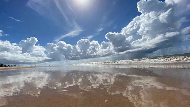 Ein Strand mit klarem Wasser, das Himmel und Wolken spiegelt.
