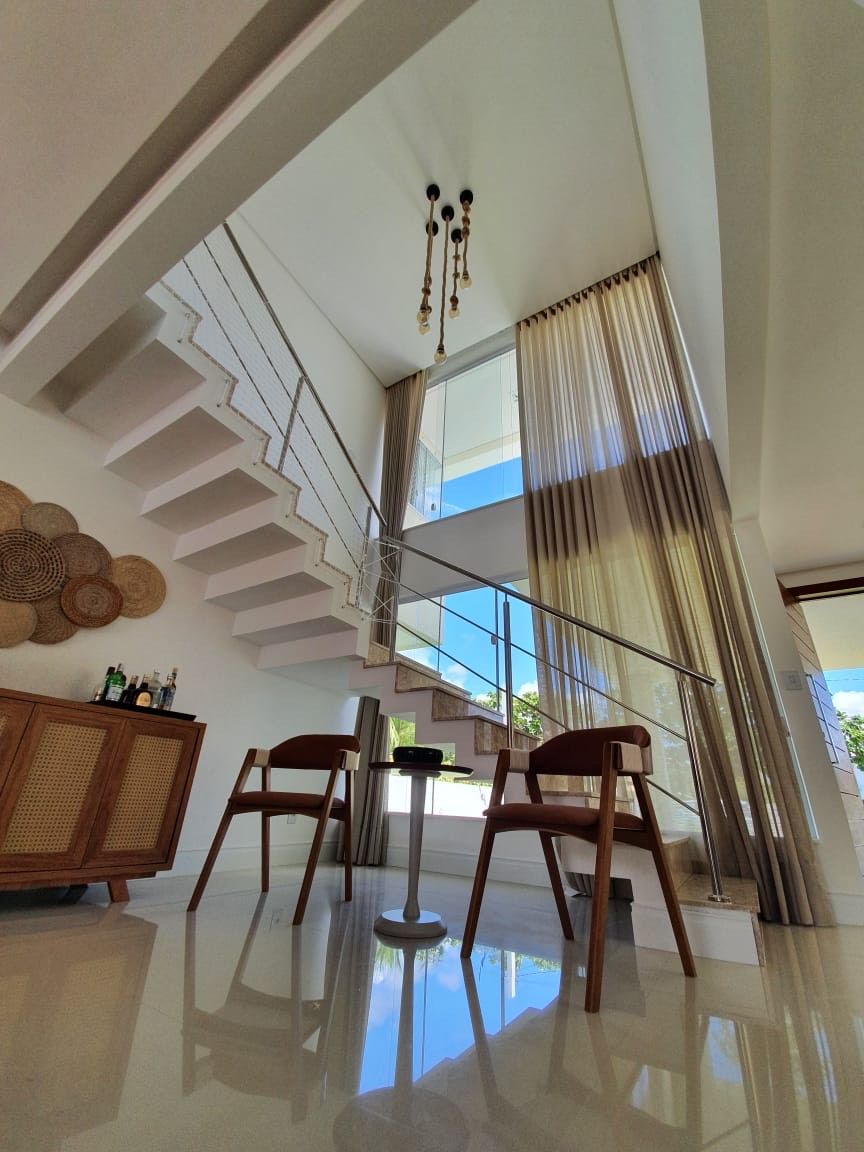 A modern interior with a staircase, a dining area with two chairs, and a large window with curtains.