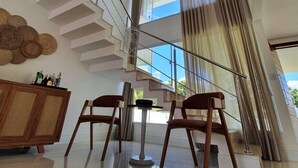 Ein modernes Interieur mit einer Treppe, einem Essbereich mit zwei Stühlen und einem großen Fenster mit Vorhängen.