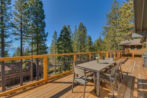 Eine Holzterrasse mit Tisch und Stühlen, mit Blick auf einen Wald und ein Gewässer.