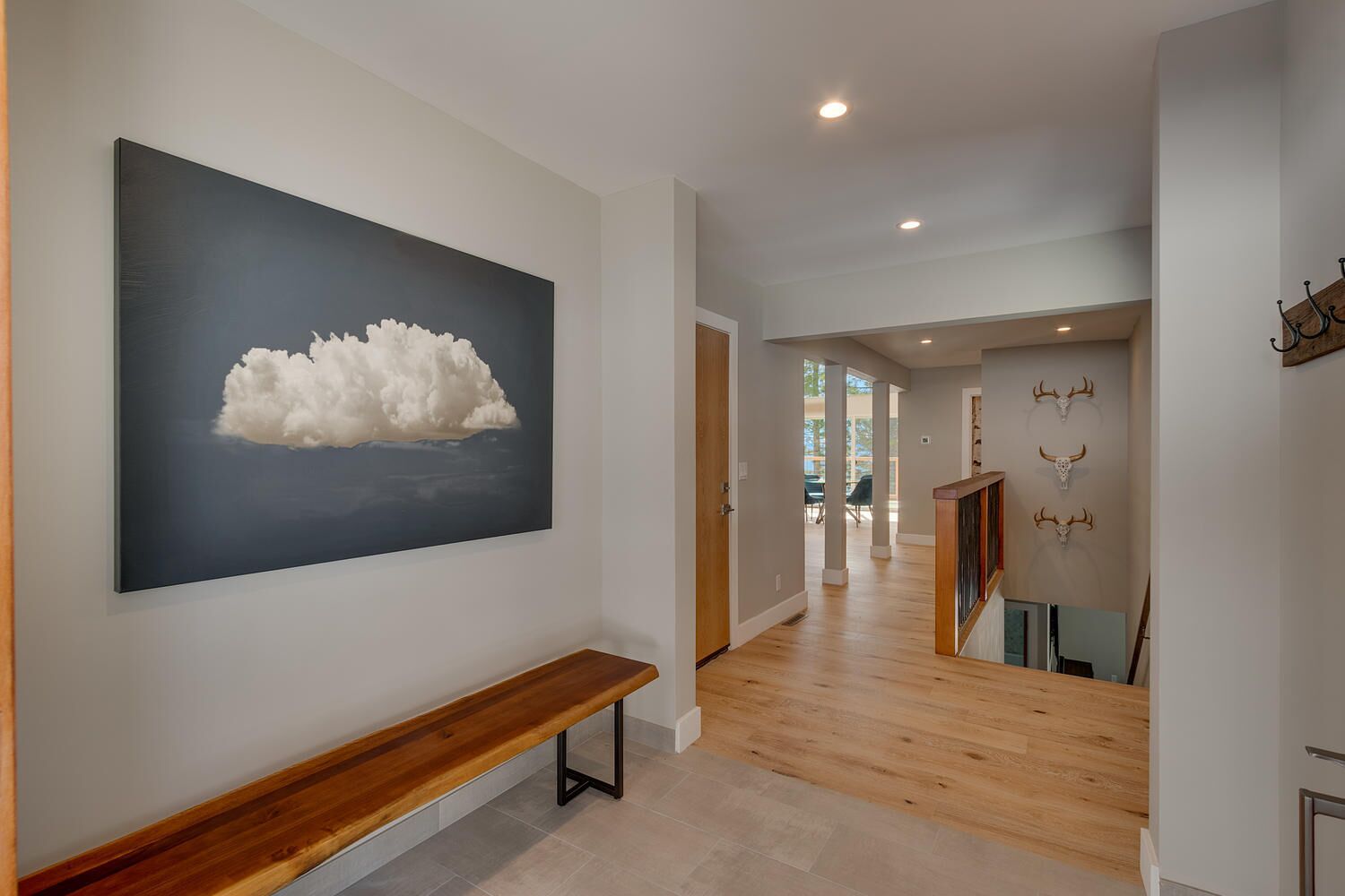 Un couloir avec un banc en bois, un grand tableau représentant un nuage accroché au mur et un escalier orné de trois crânes d’animaux.